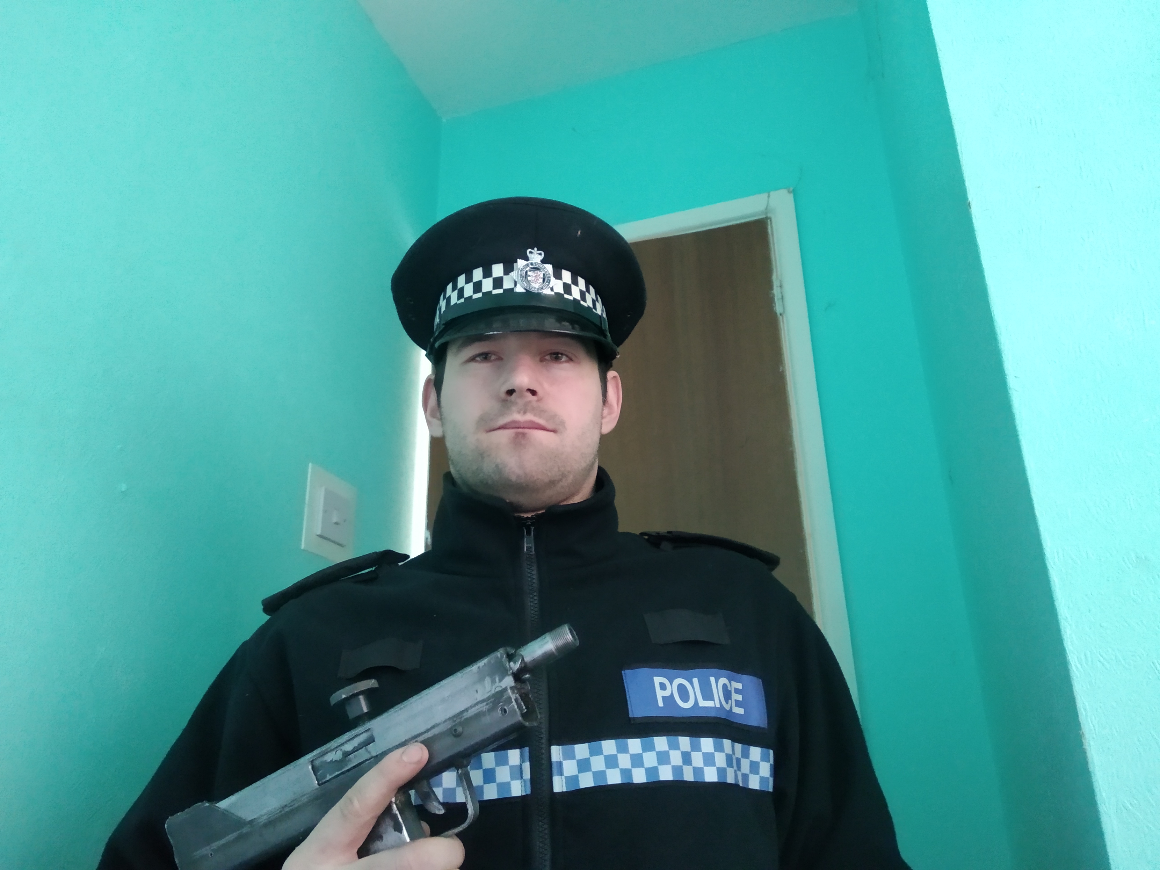 Picture of Reed Wischhusen holding a gun while wearing an Avon and Somerset Police uniform.