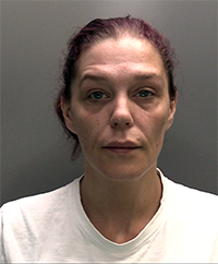 Custody photo of Sarah Campbell. She is a middle-aged white woman of slim build with dark brown hair, tied back, and blue eyes. She sits against a grey background. She is wearing a plain white t-shirt and is expressionless.