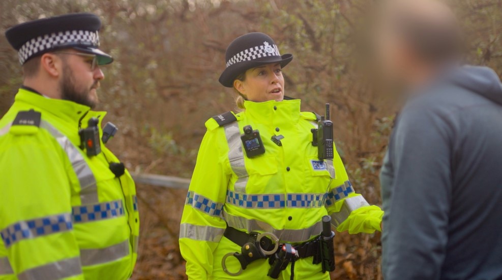 Photo of two uniformed officers in hi-vis talking to a middle-aged white man whose head and face are digitally blurred