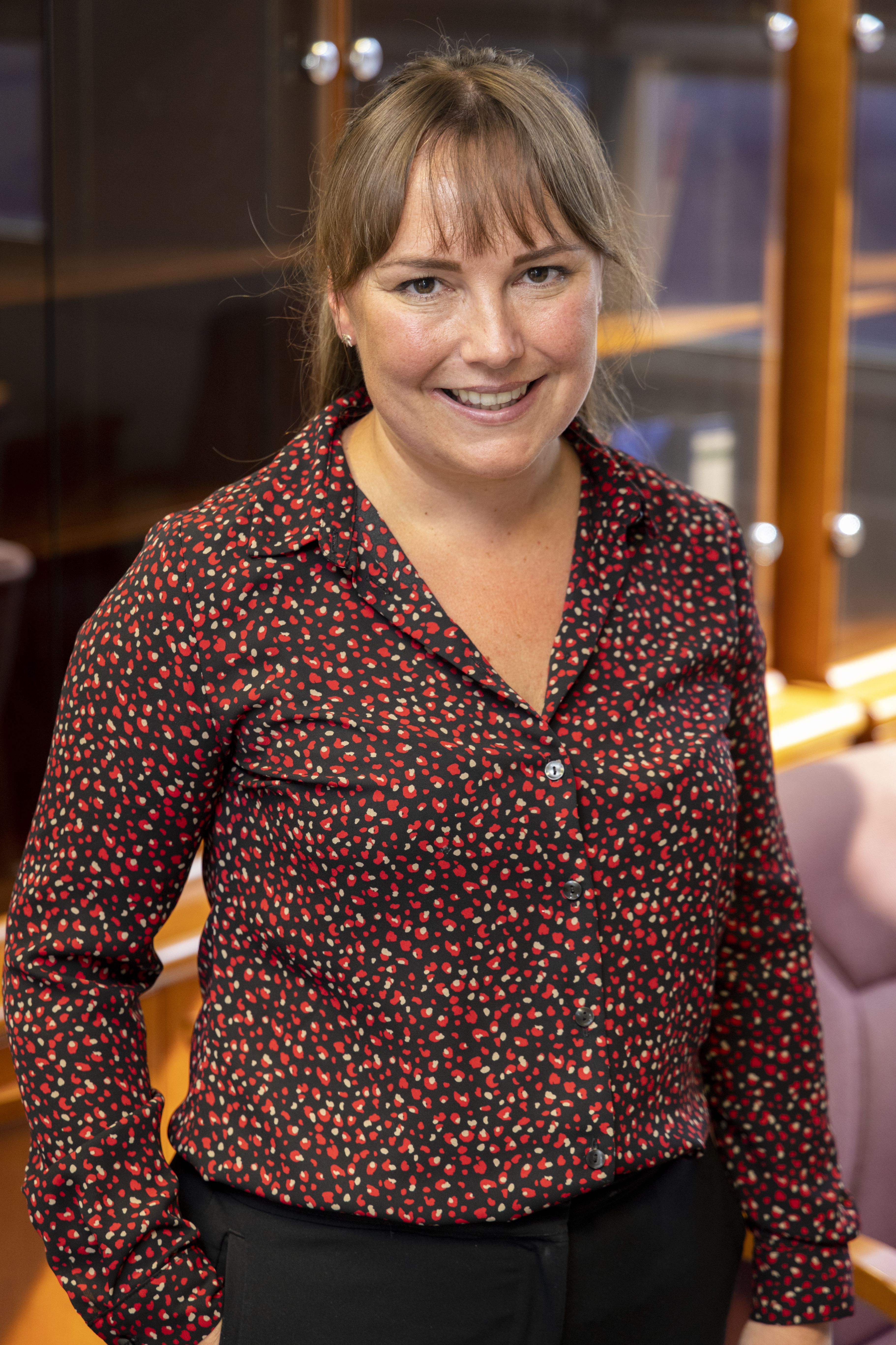 Head and shoulders photo of CPS employee Becky, Legal Manager. Brown hair with fringe, tied back, and wearing a red patterned blouse.