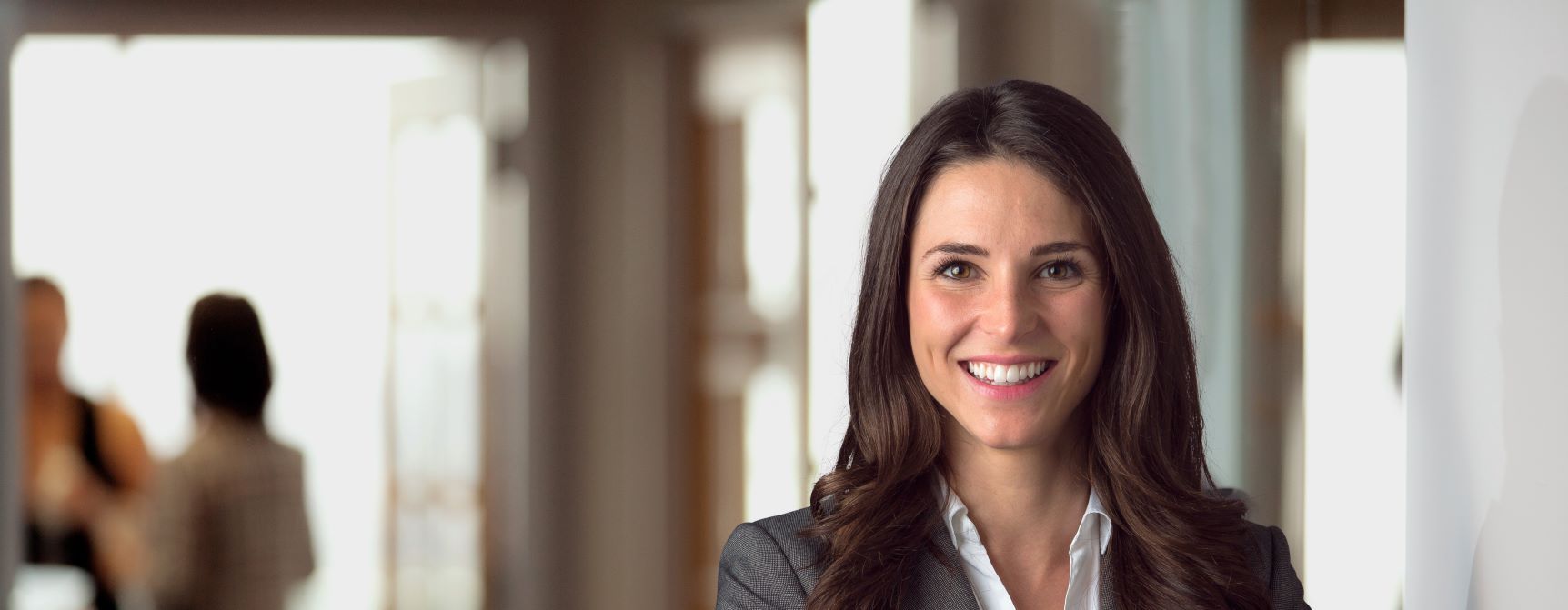 A smiling, confident-looking woman in a business suit smiles at the camera